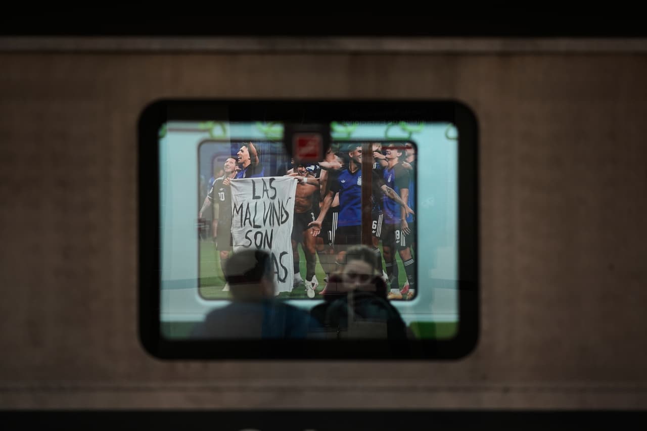 Varias personas viajan en un tren del metro detenido en una estación que muestra una foto de los futbolistas argentinos sosteniendo una pancarta con el lema "Las Malvinas son argentinas", en referencia a las Islas Malvinas, también conocidas como las Islas Falkland. La imagen fue tomada después del partido de semifinales del Mundial entre Argentina e Inglaterra, en Buenos Aires, Argentina, el lunes 27 de julio de 2026.