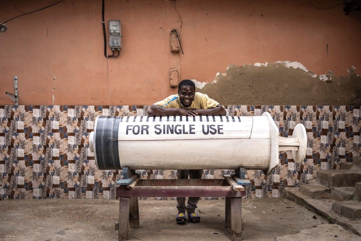 <b>Una jeringuilla para un médico:</b> Lawrence Anang, de 26 años, fabricante de ataúdes, posa junto a una de sus singulares creaciones en las inmediaciones del taller Kane Kwei, en Accra. La enorme jeringuilla fue concebida para un médico fallecido, haciendo de su profesión el motivo central de su último adiós.