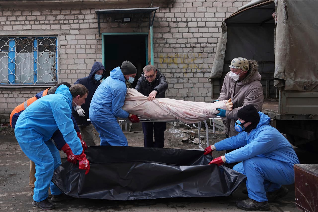 Trabajadores de una funeraria en las afueras de Mariupol mueven un cuerpo de una víctima a una bolsa de plástico. (AP Photo/Evgeniy Maloletka)