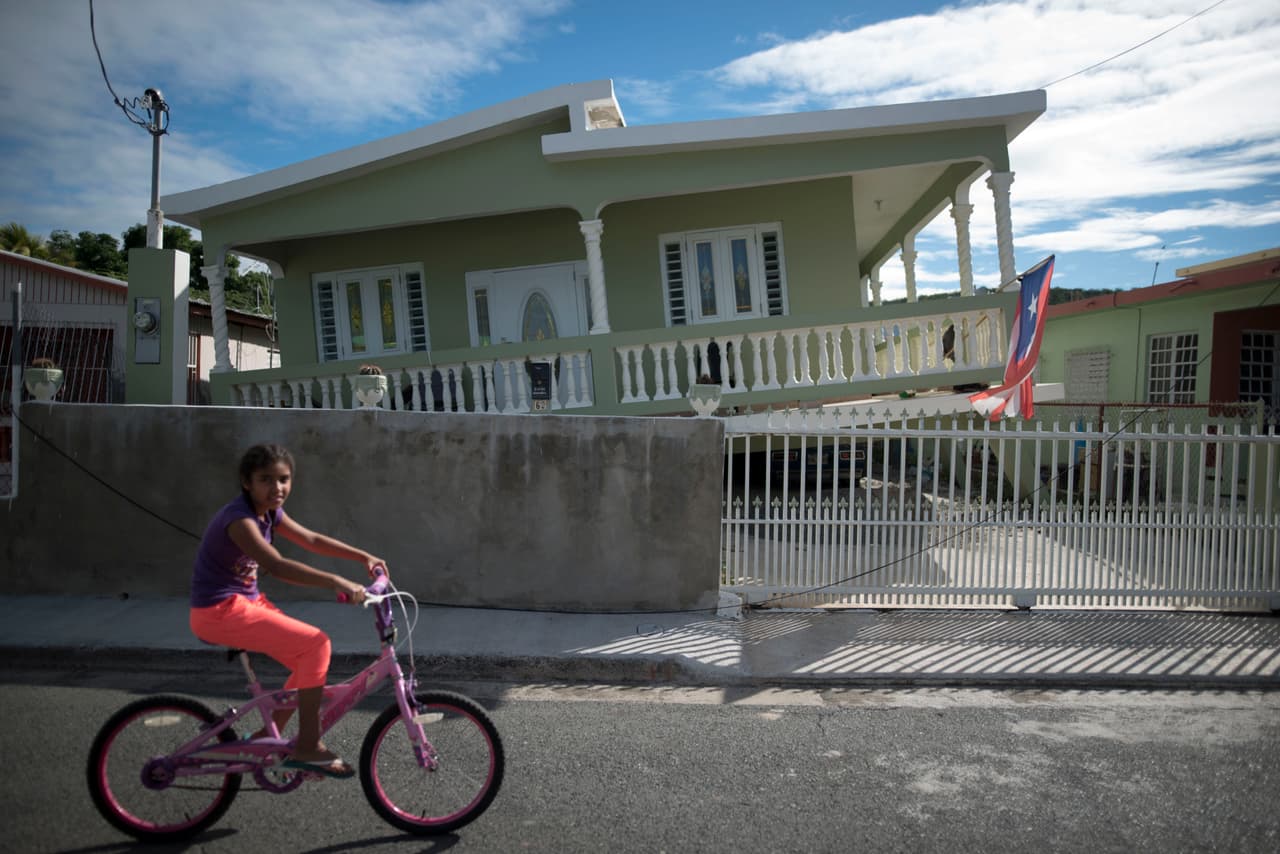 Una niña pasa en bicicleta por una casa que se derrumbó parcialmente en Guánica