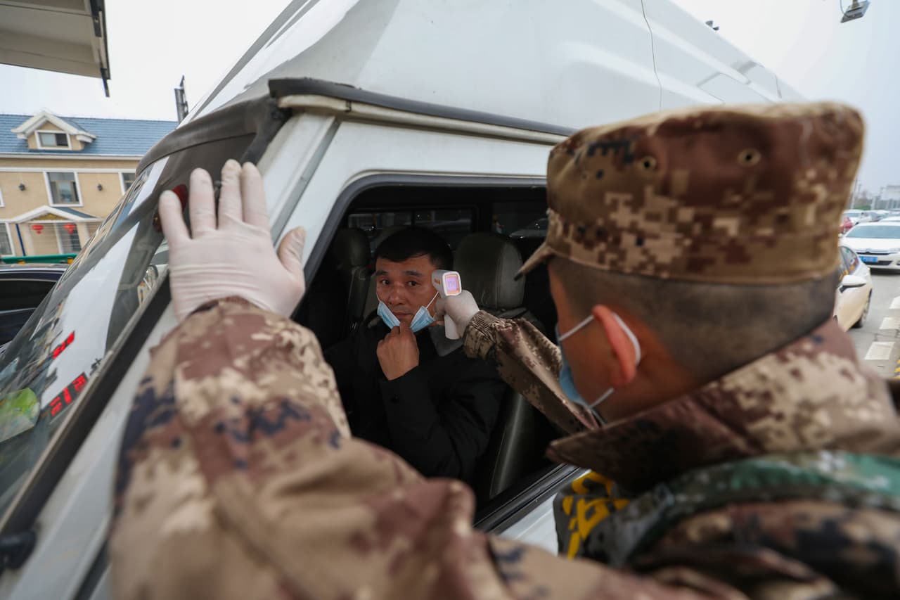 Un oficial de policía verifica la temperatura de un conductor en una carretera en Wuhan. Es obligatorio el uso de mascarillas en público y en muchas tiendas los estantes están vacíos.