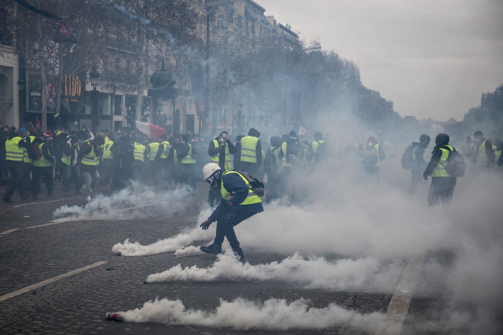 Algunos 'chalecos amarillos' toman del suelo los frascos de gas lacrimógeno que les arroja la policía para lanzarlos de regreso.