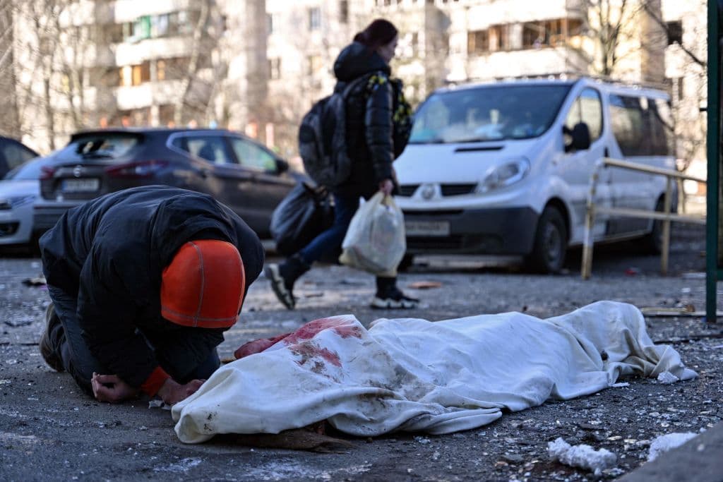 Una persona agachada junto al cuerpo del fallecido este jueves en el edificio impactado en Kiev.