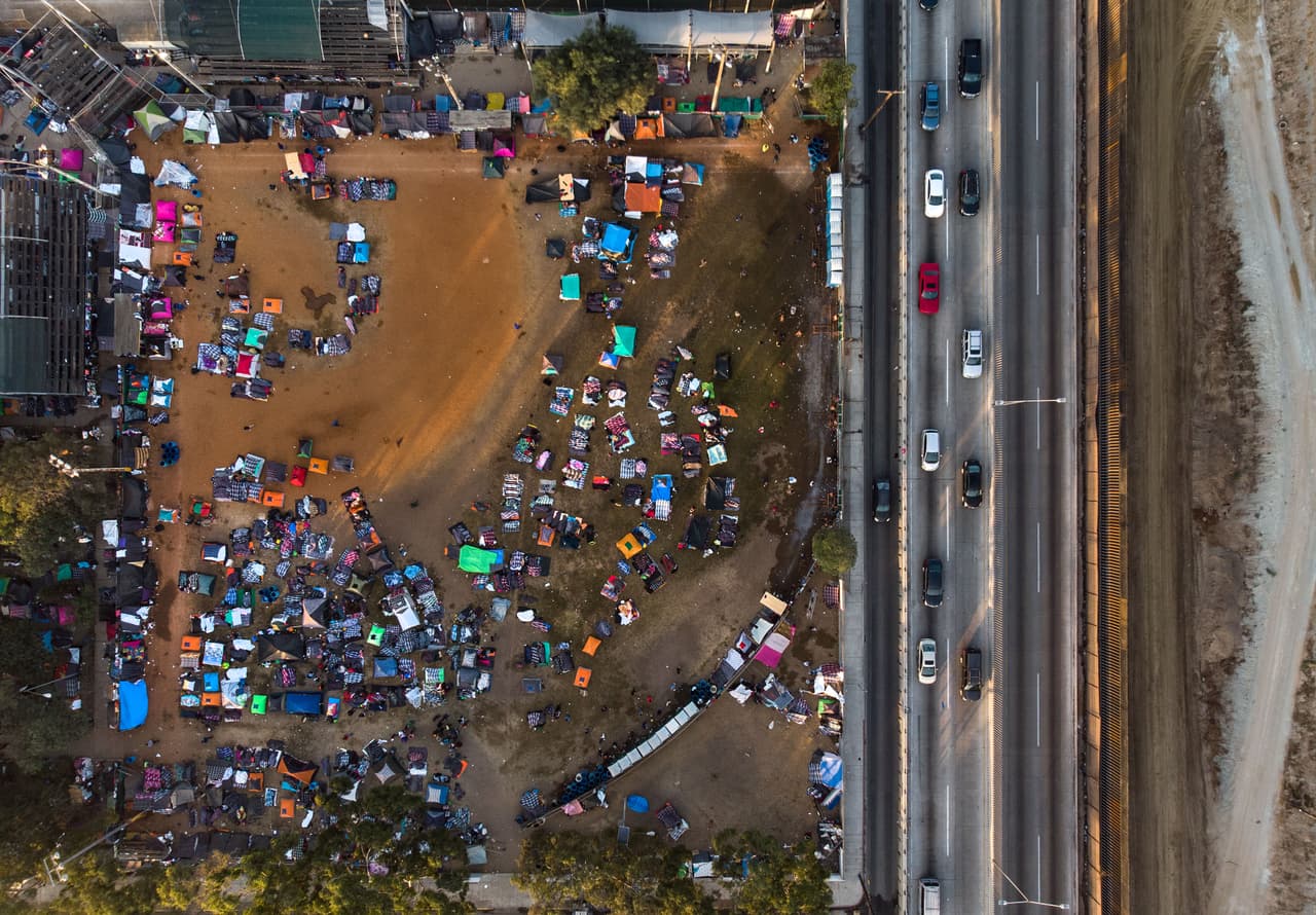 <b>Tan cerca y tan lejos. </b>El albergue instalado en la Unidad Deportiva Benito Juárez al norte de Tijuana colinda con la valla fronteriza que separa a EEUU de México. En ese refugio,
<a href="https://www.univision.com/noticias/inmigracion/sin-espacio-y-en-condiciones-precarias-asi-estan-los-migrantes-en-los-refugios-de-tijuana-fotos-fotos">sobrepasado en su capacidad de albergar migrantes, se mantienen la mayoría de centroamericanos que han llegado a Tijuana</a>. Las autoridades calculan que más personas llegarán a la ciudad y permanecerán ahí varias semanas. 21 de noviembre de 2018.