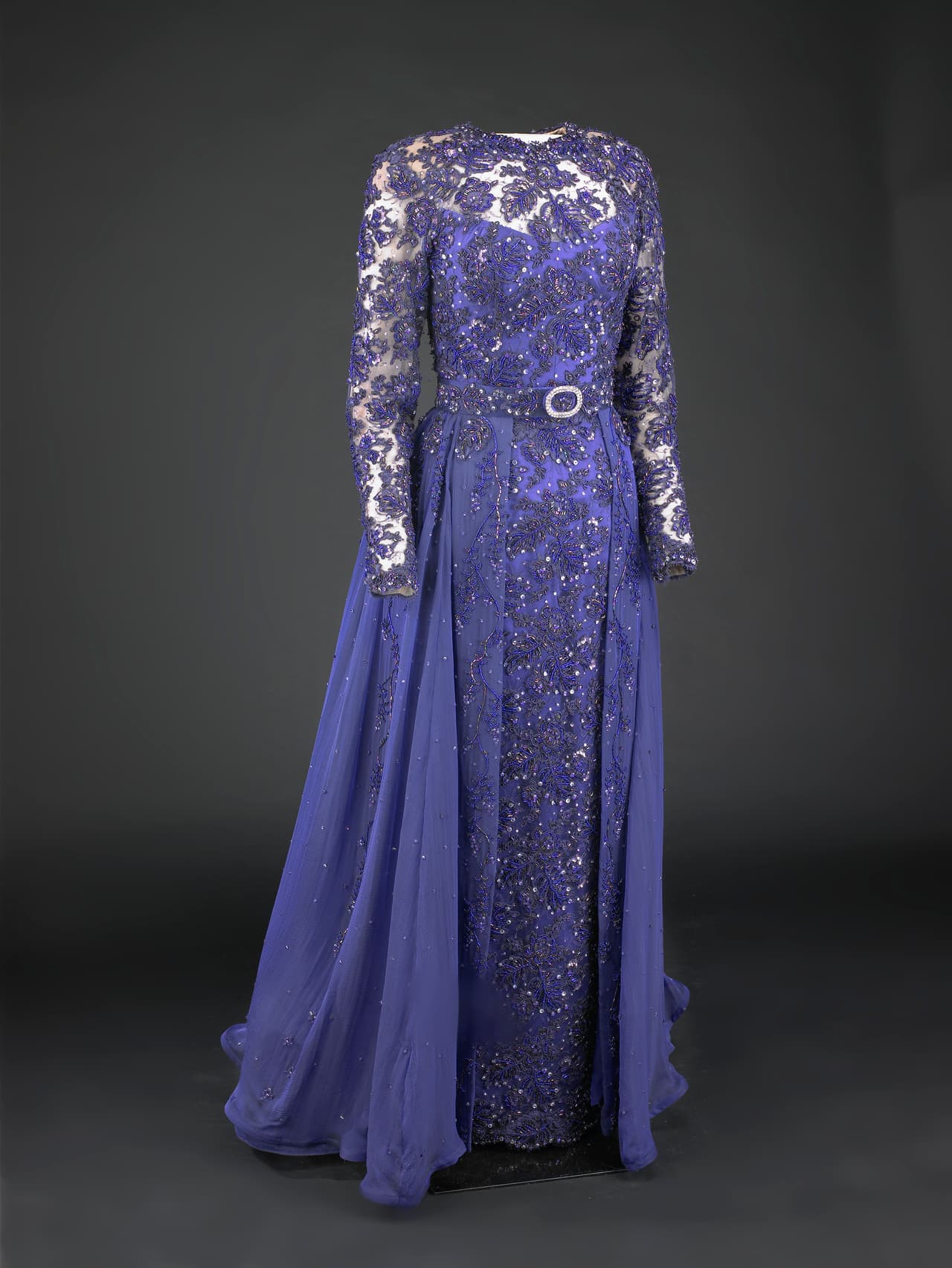 El vestido púrpura de encaje y brocado y con unas iridisencias azules fue efectivamente diseñado por
<b>Sarah Phillips</b> pero fue hecho por la casa Barabara Matera, una afamada productora de vestidos de teatro de Nueva York. Sus zapatos fueron de Bruno Magli y su clutch Judith Leiber.