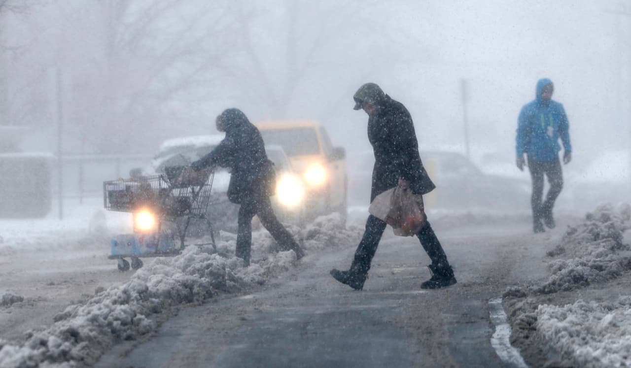 Compradores luchan por regresar a los vehículos estacionados afuera de una tienda de comestibles mientras la tormenta de invierno azota Denver.