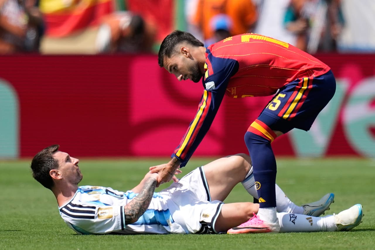 Alex Baena ayuda a Messi a levantarse después de una caída ocasionada por una jugada.