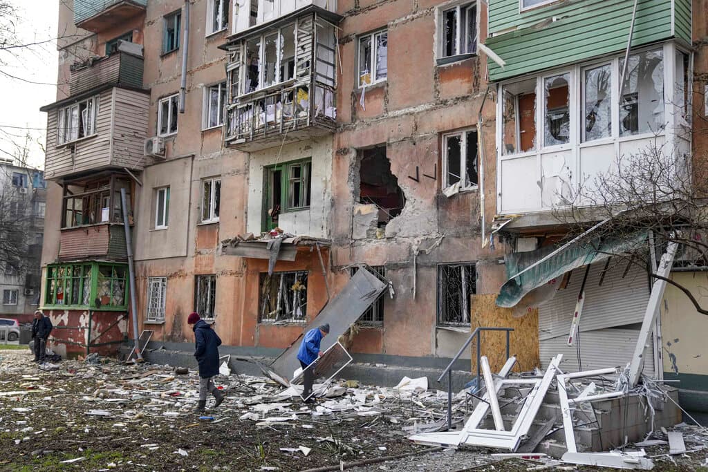 La gente camina junto a un edificio de apartamentos alcanzado por los bombardeos en Mariupol, Ucrania.