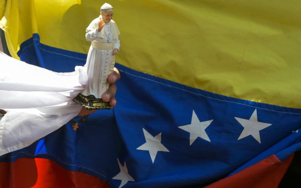 TOPSHOT - A faithful holds a souvenir doll of Pope Francis next to a Venezuelan national flag, while gathering alongside the street to see him, during the World Youth Days in Panama City on January 24, 2019. - Pope Francis will on Thursday formally open World Youth Day celebrations which have drawn around 200,000 young people from around the world to Panama where he is expected to defend Central American migrants and human rights. (Photo by Raul Arboleda / AFP) (Photo credit should read RAUL ARBOLEDA/AFP/Getty Images)