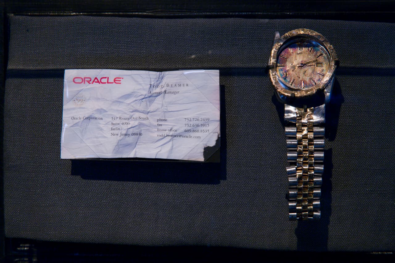 Una tarjeta de presentación y el reloj que llevaba Todd Beamer, un ejecutivo de Oracle Corporation que falleció en el vuelo 93 de United Airlines. El avión cayó a tierra cerca de Shanksville, Pennsylvania, cuando un grupo de pasajeros,
<a href="http://www.dba-oracle.com/t_hero_todd_beamer.htm"><u>entre ellos Beamer, lucharon con los terroristas para retomar el control de la aeronave</u></a>.