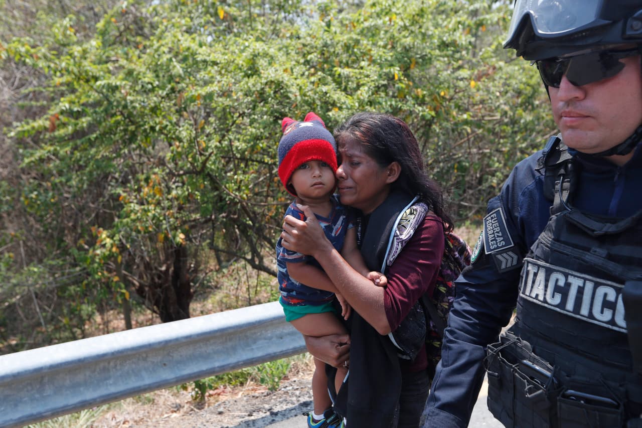 Agentes federales detuvieron a cientos de migrantes en el sur de México que iban en caravana rumbo al norte en el mayor operativo del que se tiene noticia desde que miles de centroamericanos optaron por migrar en caravana rumbo a EEUU. En la fotografía una madre centroamericana y su hijo custodiada por un agente de la Policía federal mexicana en Pijijiapan, estado de Chiapas.