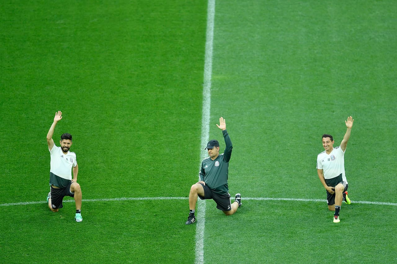 Oribe Peralta (izq) y Andrés Guardado (der) con rodilla en tierra y con el brazo estirado obedecen las órdenes del preparador físico del equipo mexicano. Palpando el terreno y soltando el músculo.