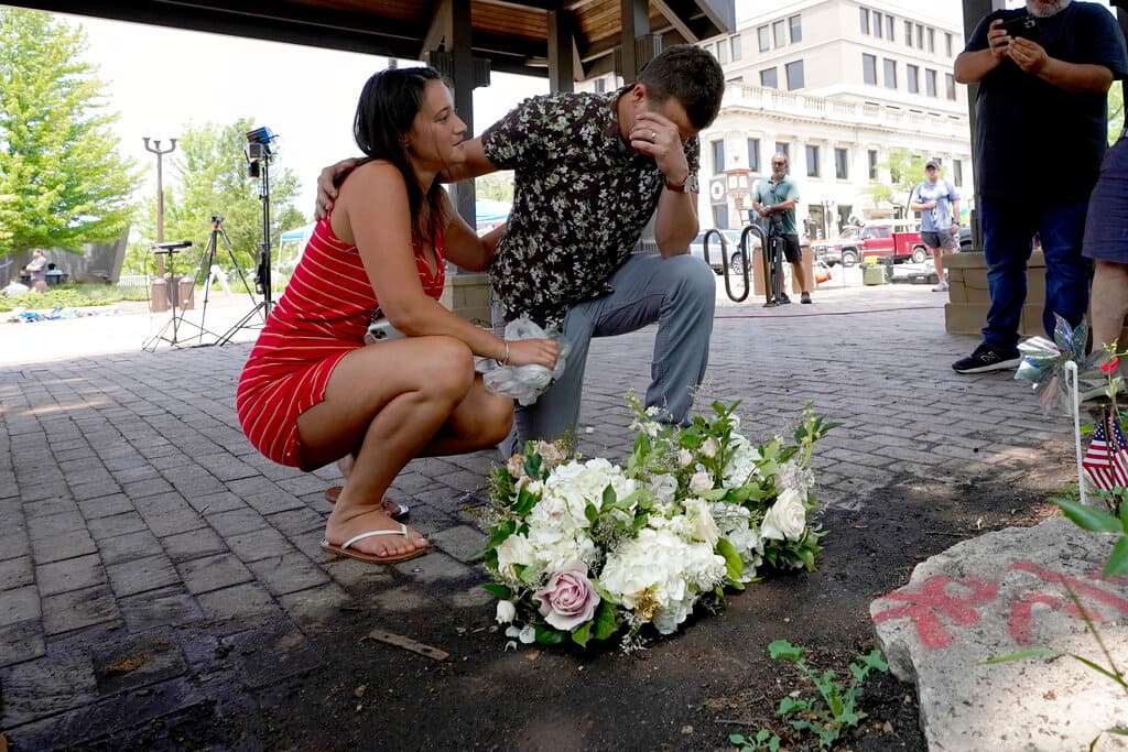 Brooke y Matt Strauss, que se casaron el domingo, hacen una pausa el martes 5 de julio de 2022 después de dejar sus ramos de boda en el centro de Highland Park, Illinois, un suburbio de Chicago, cerca de la escena de la masacre del lunes.