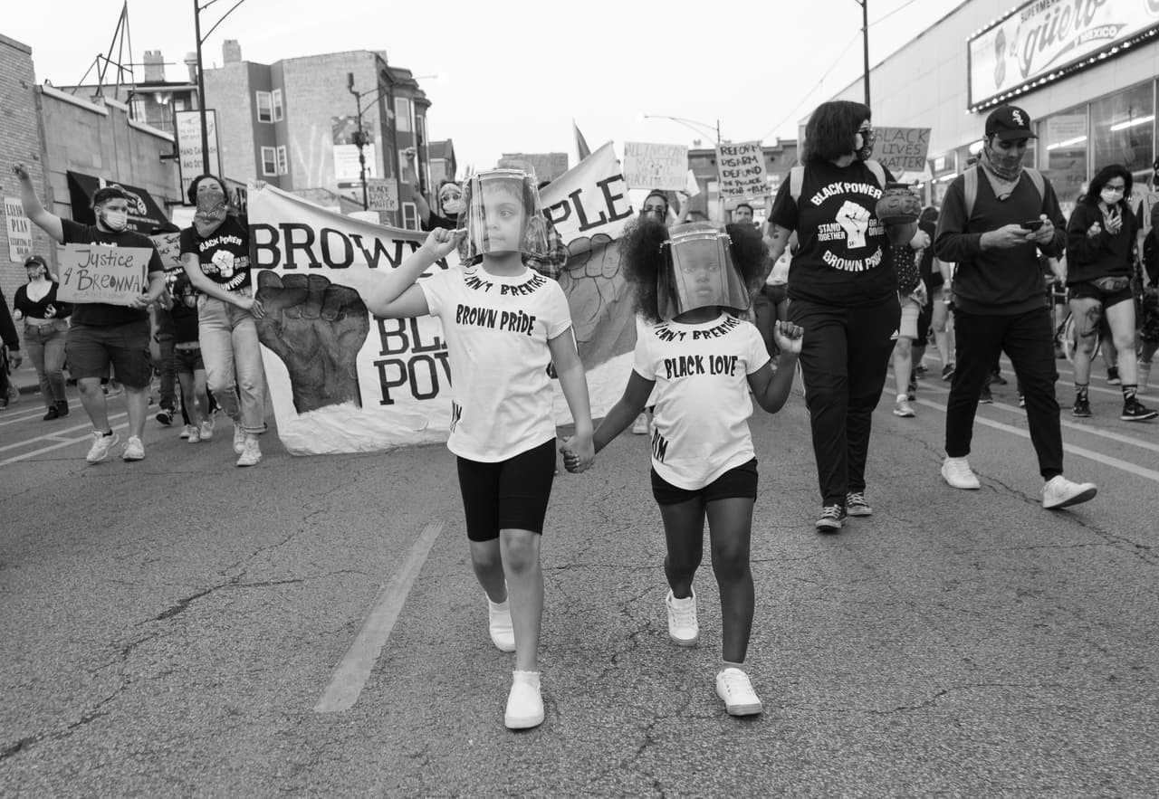 Fotografía del 2 de junio en la marcha "Black and Brown Unity March" en Pilsen. Esta marcha se organizó para reafirmar la solidaridad de la comunidad latina con el movimiento "Black Lives Matter". En la fotografía aparecen Nivea Sandoval, una niña latina, y Tia James, una niña afroamericana, de la mano marchando.
