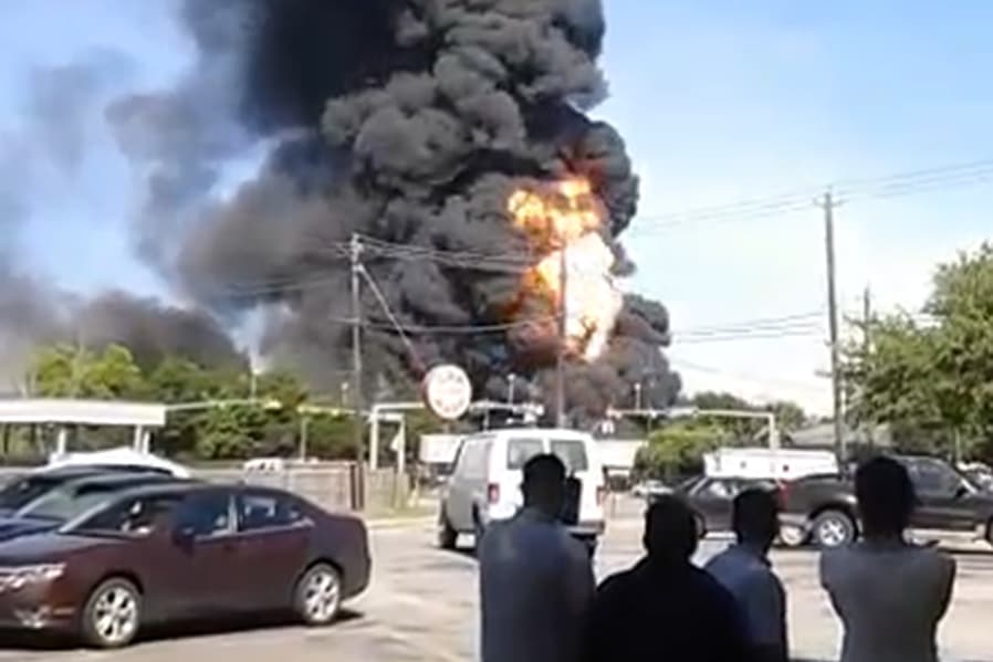 Empleados de varios locales comerciales observan atónitos la gigantezca nube de humo de un masivo incendio al noroeste de Houston.