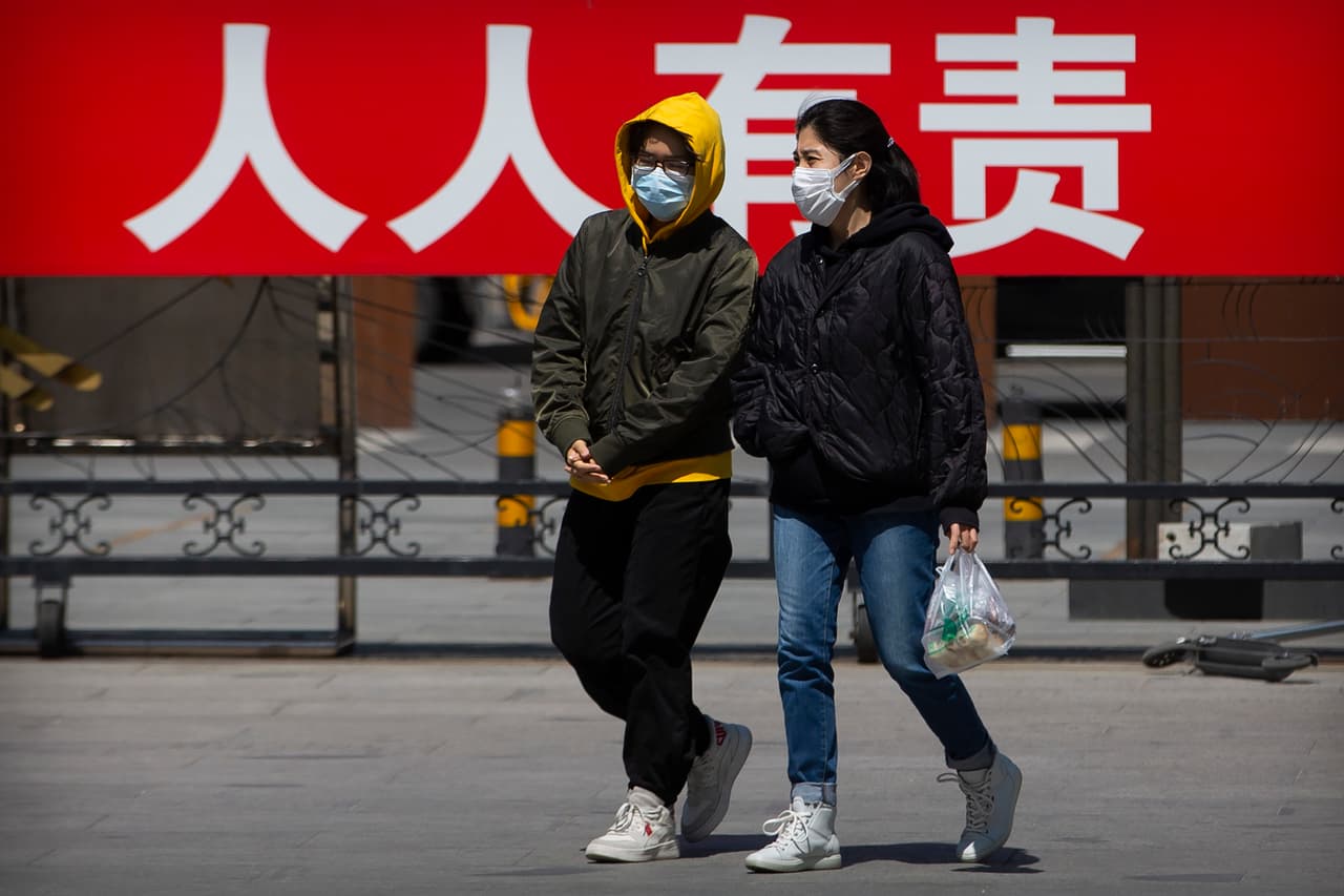 Dos personas caminan con mascarillas frente a un cartel propagandístico en Pekín en el que se lee: "es responsabilidad de todos controlar el contagio de esta enfermedad".