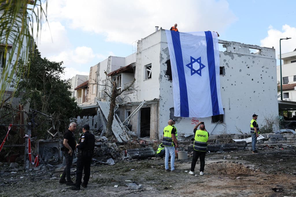 Un trabajador de emergencia toma una fotografía de una bandera israelí desplegada en la pared de un edificio dañado en Kiryat Bialik, en el distrito de Haifa, tras un de Hezbollah este domingo.