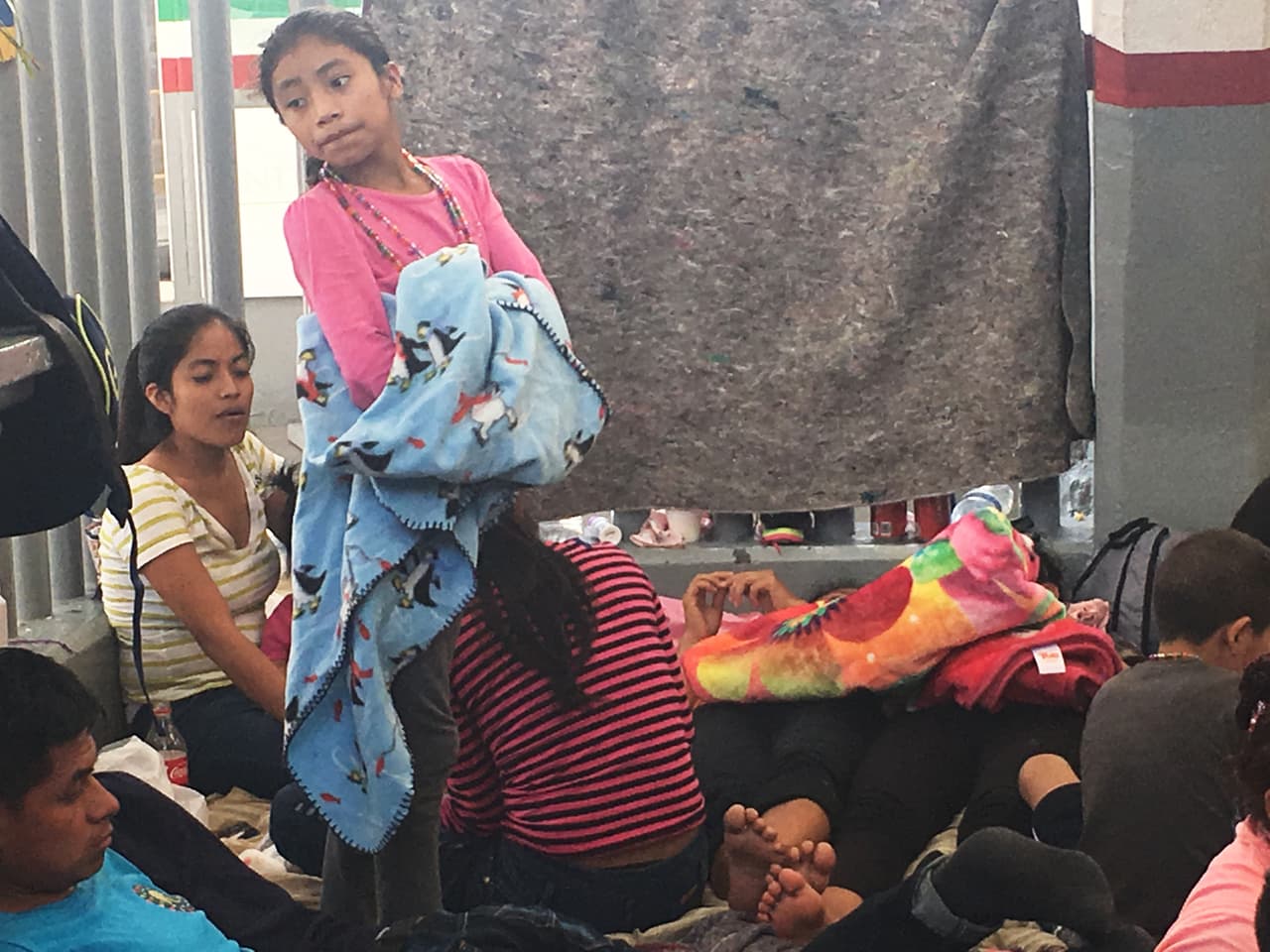 Niños de todas las edades con sus padres esperan en el piso entre cobijas y comida para cruzar a Estados Unidos