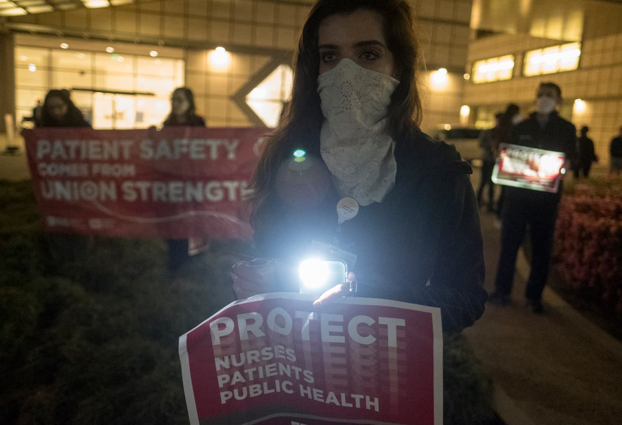 Una enfermera del Centro Médico Ronald Reagan de la UCLA sostiene un teléfono inteligente para iluminar una pancarta en la que piden protección para el personal sanitario, los pacientes y los centros públicos de atención sanitaria.