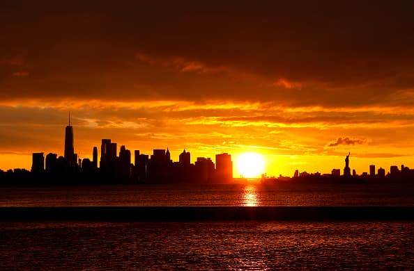 El sol sorprende detrás del horizonte del bajo Manhattan, One World Trade Center y la Estatua de la Libertad.