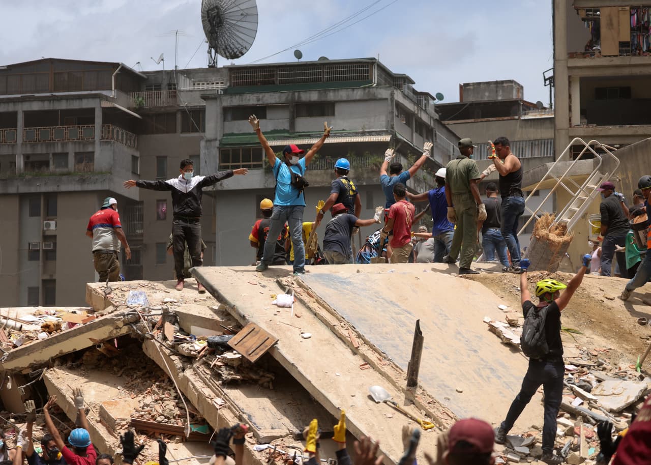 Varias personas hacen gestos mientras buscan víctimas entre los escombros de un edificio derrumbado, tras los terremotos en Caracas.