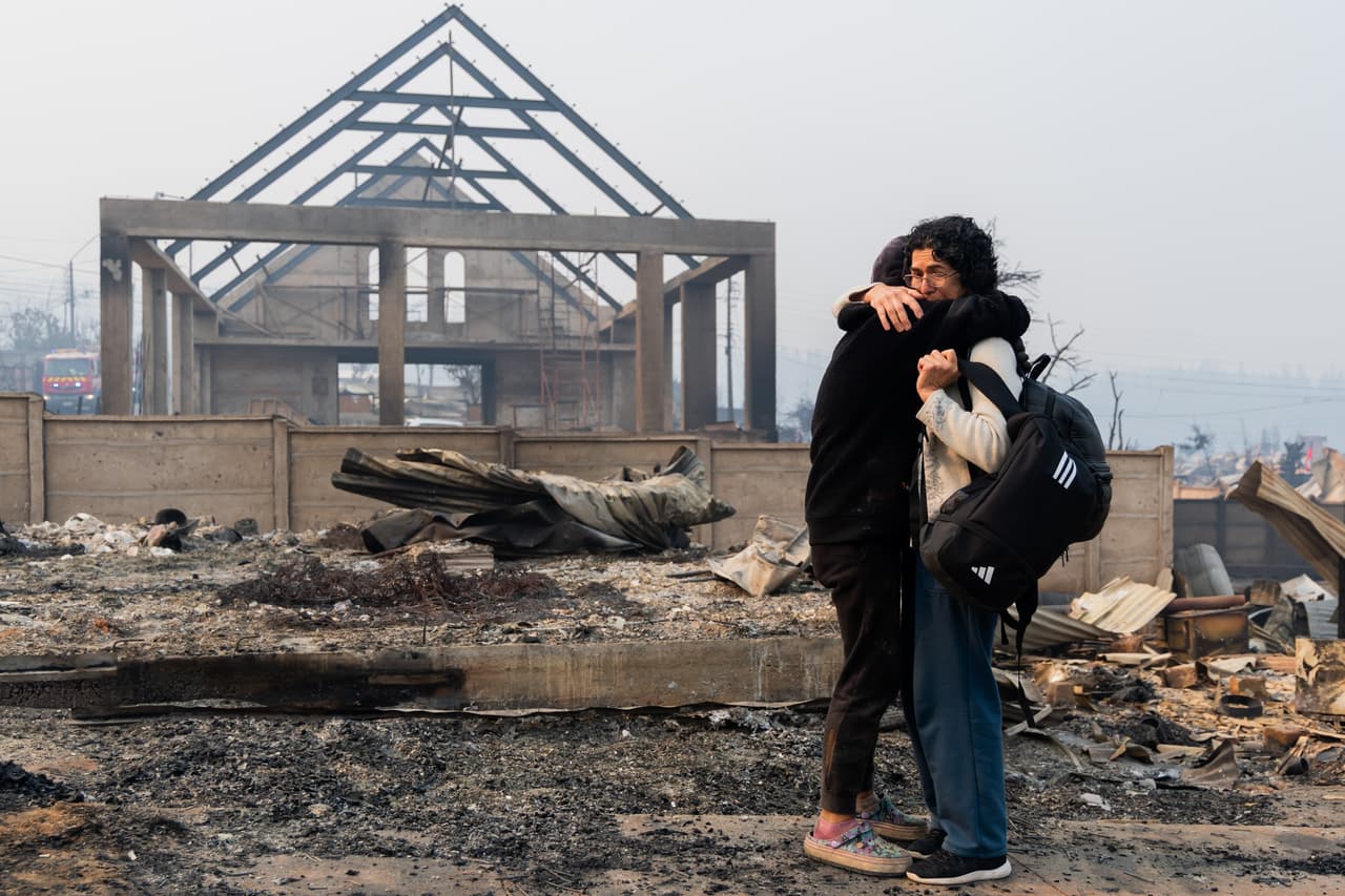 Una madre y su hija se abrazan frente a su casa quemada por los incendios forestales en Tomé, Chile.