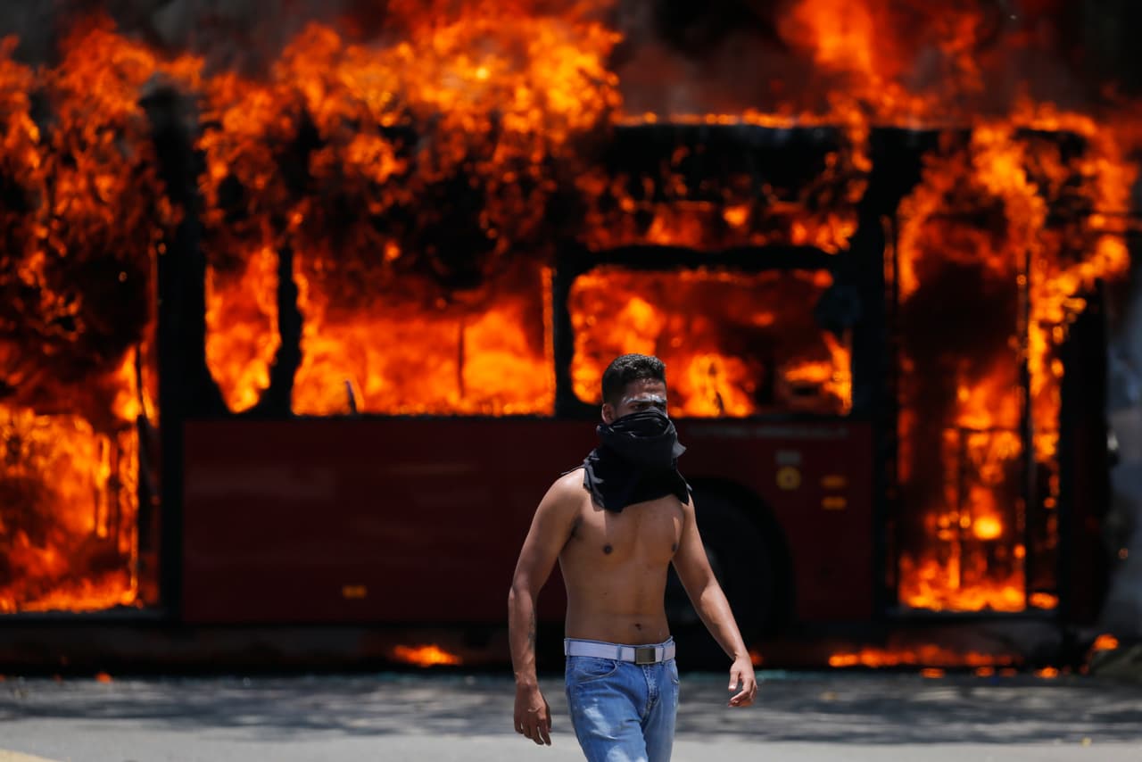 Un manifestante antigubernamental camina cerca de un autobús que fue incendiado por opositores a Maduro.
