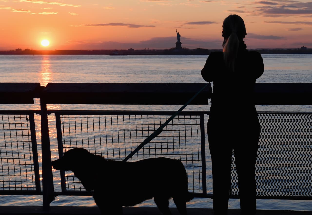 Una mujer toma una fotografía del atardecer mientras pasea a su perro.