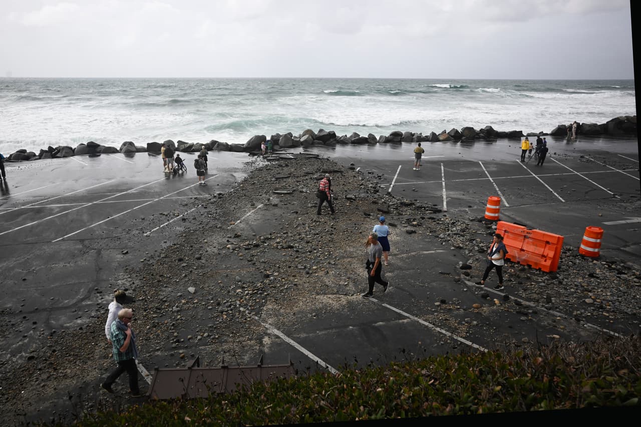 Varias personas caminan por el estacionamiento cerrado de la playa estatal Tamarack en Carlsbad, California, el domingo 11 de octubre de 2026, debido a la tormenta tropical Rachel.