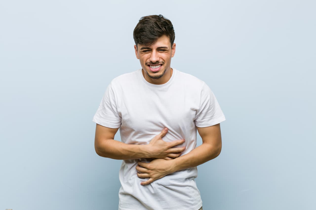 Young caucasian man wearing a white tshirt sick, suffering from stomachache, painful disease concept.