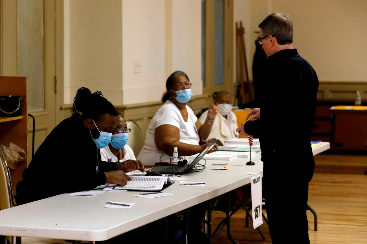 En esta fotografía se observa a trabajadores electorales usando mascarillas faciales mientras ayudan a votantes en una iglesia protestante en la ciudad de Detroit, Michigan.