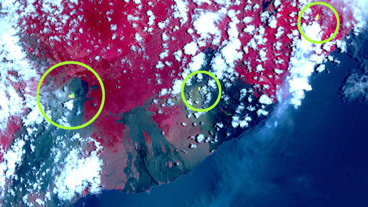 Esta fotografía suministrada por NASA fue tomada por el Radiómetro de Emisión y Reflexión Térmica Avanzado, que va a bordo de un satélite. Las áreas rojas en la imagen son vegetación y las áreas negras y grises son antiguos flujos de lava. Los puntos amarillos superpuestos sobre la imagen (en los círculos) muestran los puntos calientes que fueron detectados por el satélite. A la izquierda el cráter principal y a la derecha la fisura más nueva que está causando problemas en un área residencial.