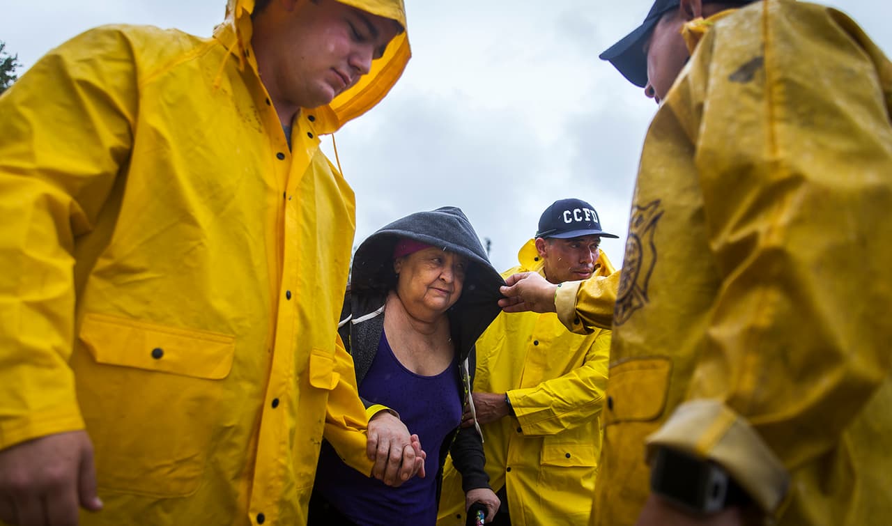 Bomberos de Corpus Christi ayudan a Guadalupe Guerra, quien tomará un autobús que la llevará a un lugar a salvo en San Antonio, Texas, en un centro de evacuación de la ciudad.