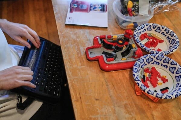 Matthew Shifrin, fundador de Bricks for the Blind, lee en un lector de braille mientras construye un proyecto de Lego en la casa de su familia, el viernes 20 de marzo de 2026, en Newton, Massachusetts.
<br>