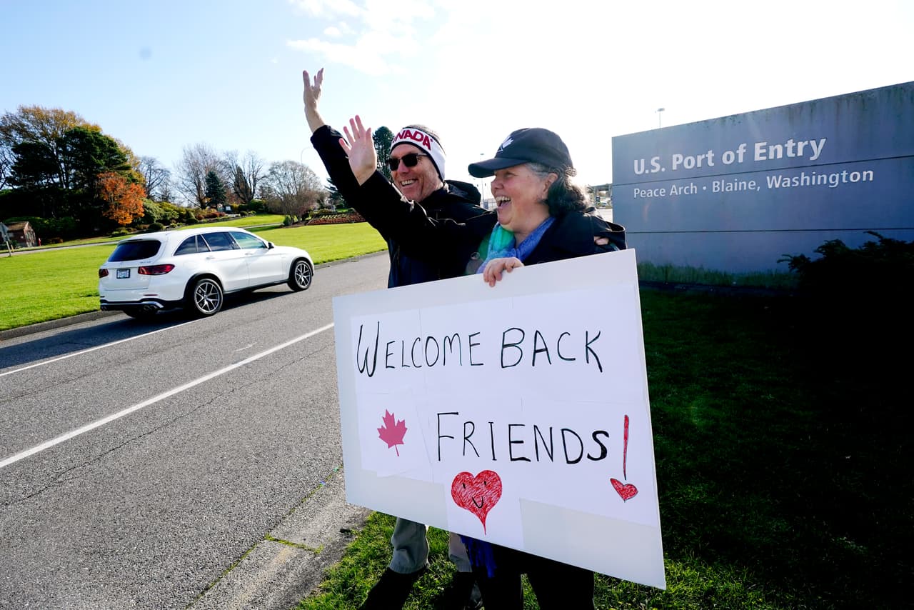 Traysi Spring, quien tiene ciudadanía estadounidense y canadiense junto a su esposo Tom Bakken (estadounidense). Sostienen un cartel que da la bienvenida a las personas que van entrando desde Canadá por un puesto fronterizo en Blaine, Washingto