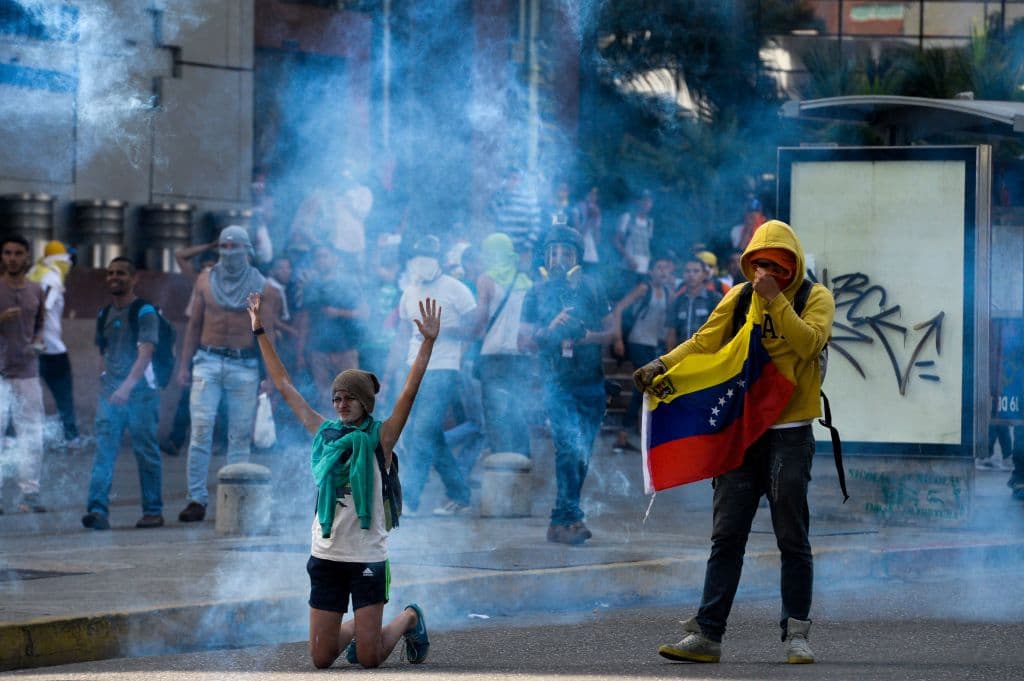 Opositores el régimen de Nicolás Maduro se cubren el rostro para resisitir los gases lacrimógenos lanzados por la policía.