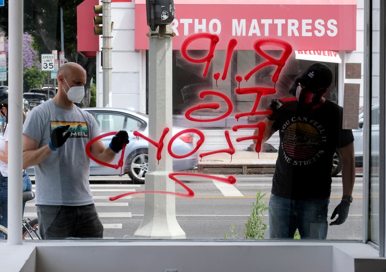 Voluntarios limpian los graffitis en las vitrinas de varios locales comerciales en Los Ángeles.
