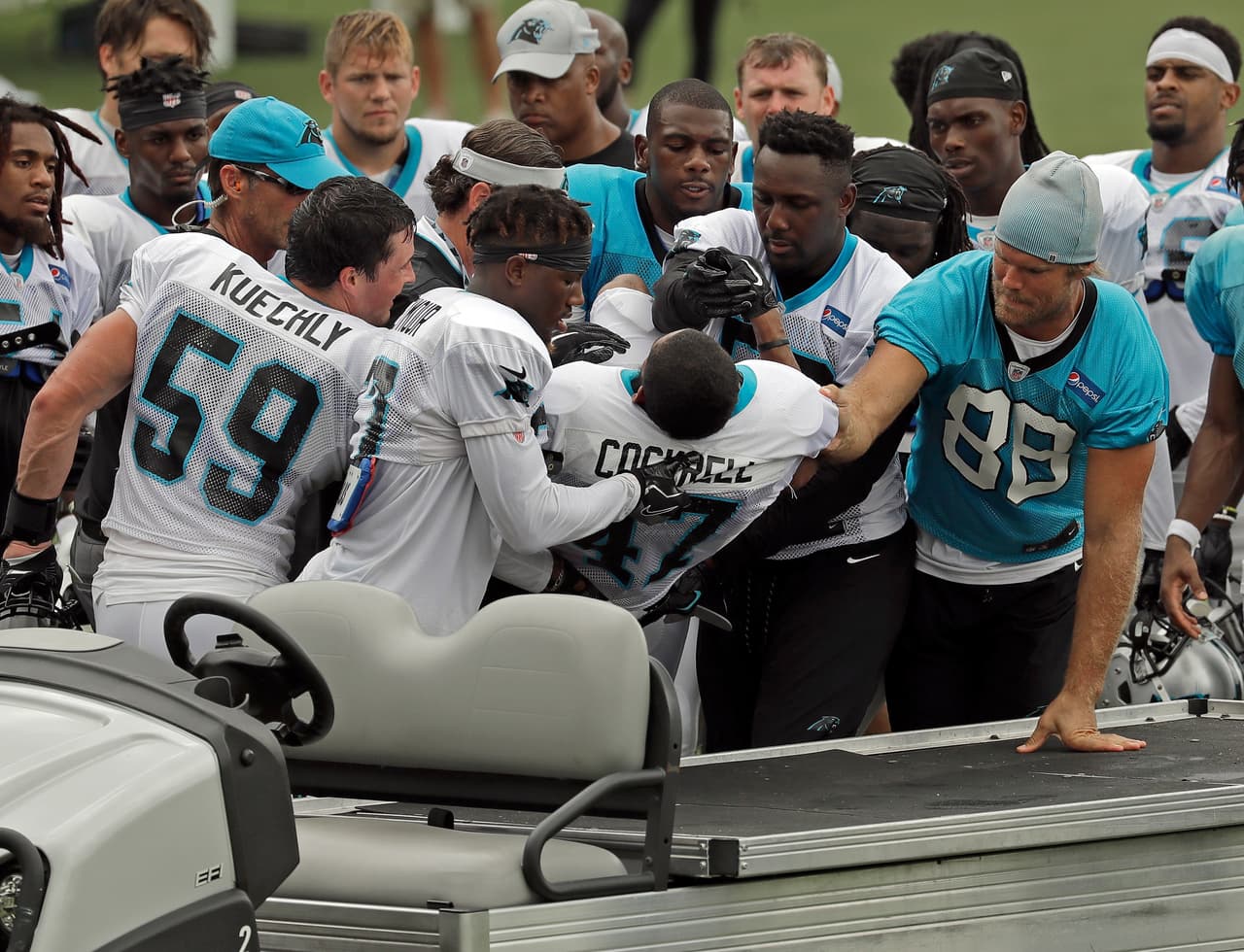 Varios jugadores de los Carolina Panthers como Luke Kuechly (59) y Greg Olsen (88) ayudan a que Ross Cockrell (47) sea puesto en un vehículo y sea atendido tras lesionarse en la práctica del equipo.
