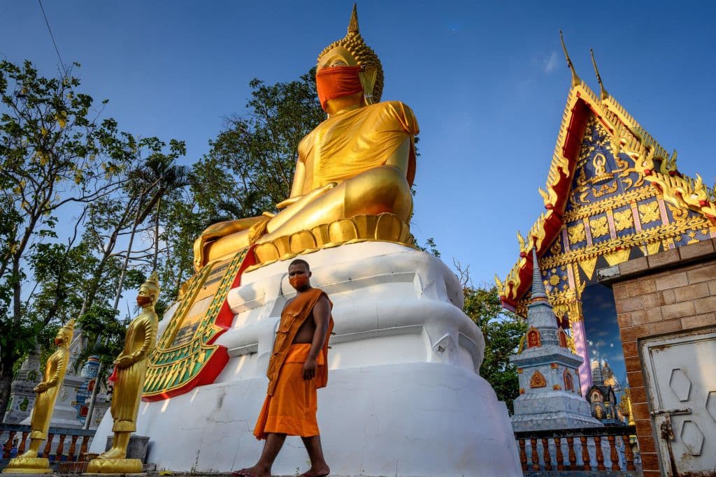 Un monje camina frente a una estatua gigante de Buda con una máscara facial de color naranja en el templo Wat Nithet Rat Pradit.
