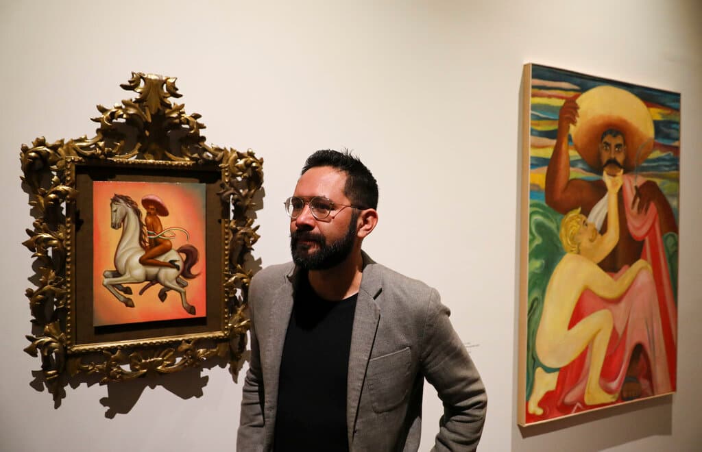 El curador mexicano Luis Vargas junto a una pintura que muestra a Emiliano Zapata montando desnudo.