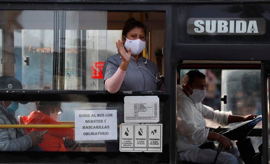 Una mujer usando una máscara facial saluda desde un bus en Lima (Perú).