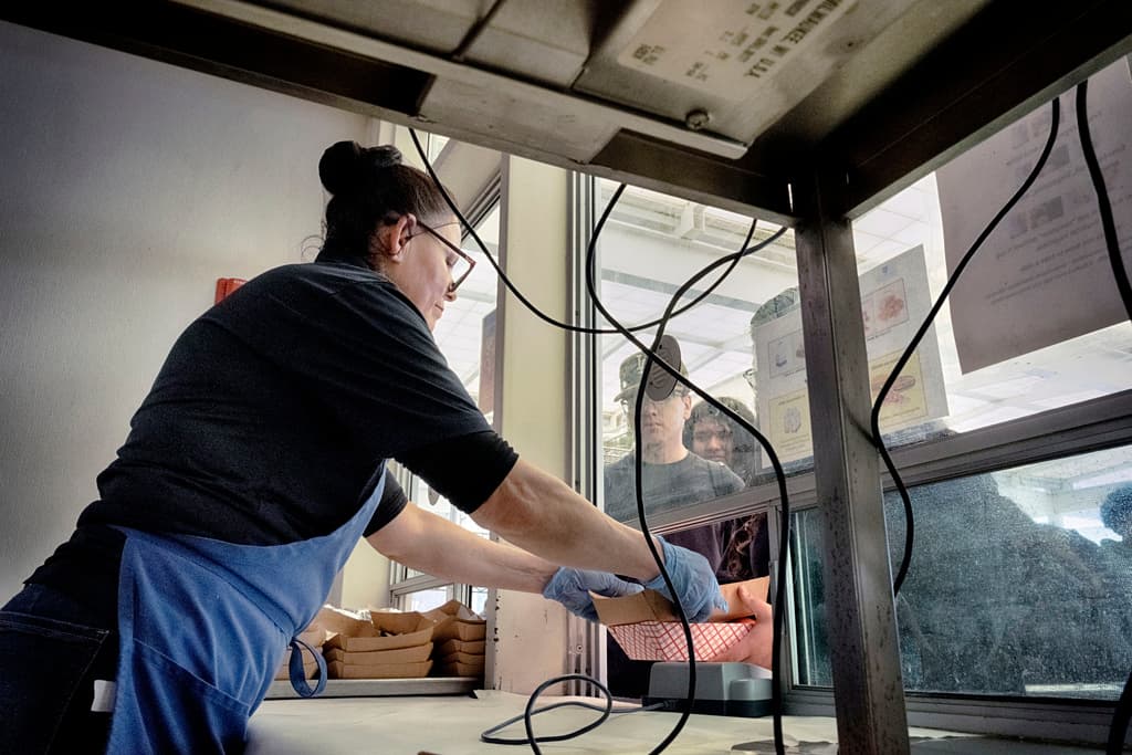 Nuria Alvarenga, empleada de la cafetería, sirve el almuerzo a los estudiantes a través de una ventanilla de servicio en la escuela secundaria Firebaugh de Lynwood, California, el miércoles 3 de abril de 2024.