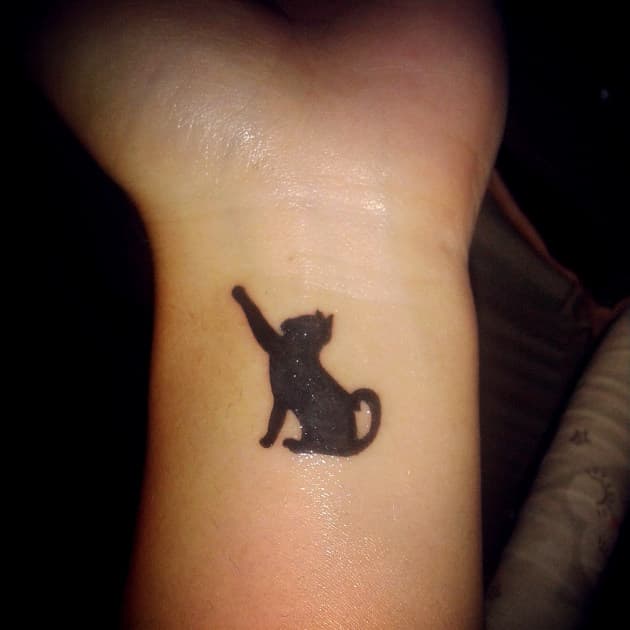 El delicado tatuaje de gato negro en la muñeca de Andrea